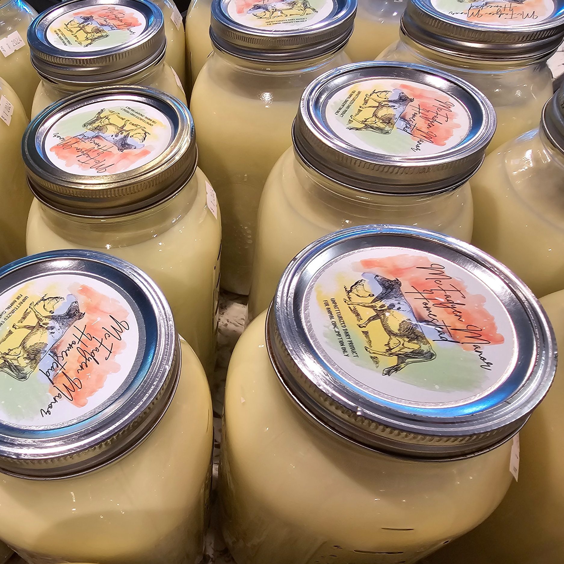 Jars of homemade creamy dairy products with colorful, artistic labels, arranged closely together on a countertop, showcasing a farm-fresh aesthetic.